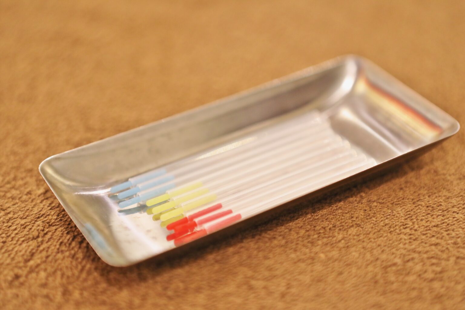 Fine single-use acupuncture needles resting in their colour-coded guide tubes on a stainless steel tray